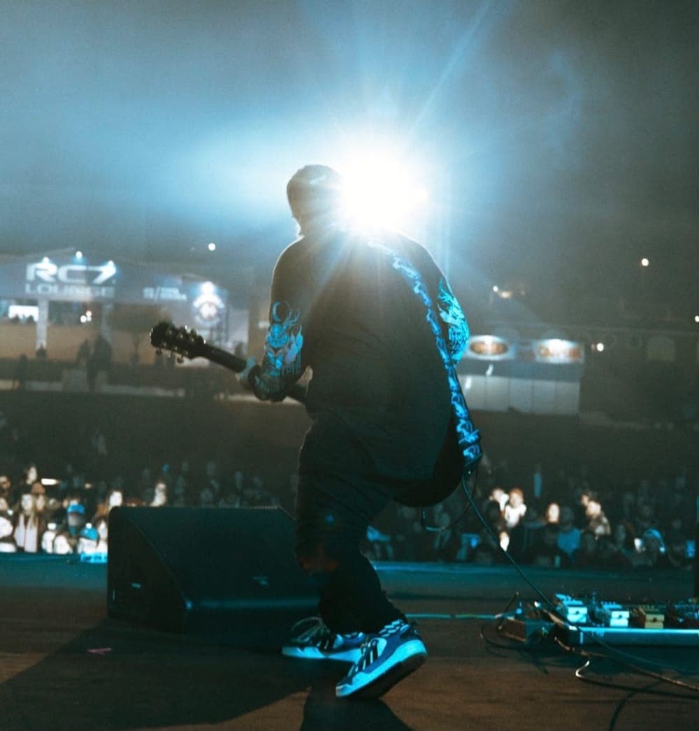 Mateus Rosa de costas no palco, com a guitarra, de frente para o público