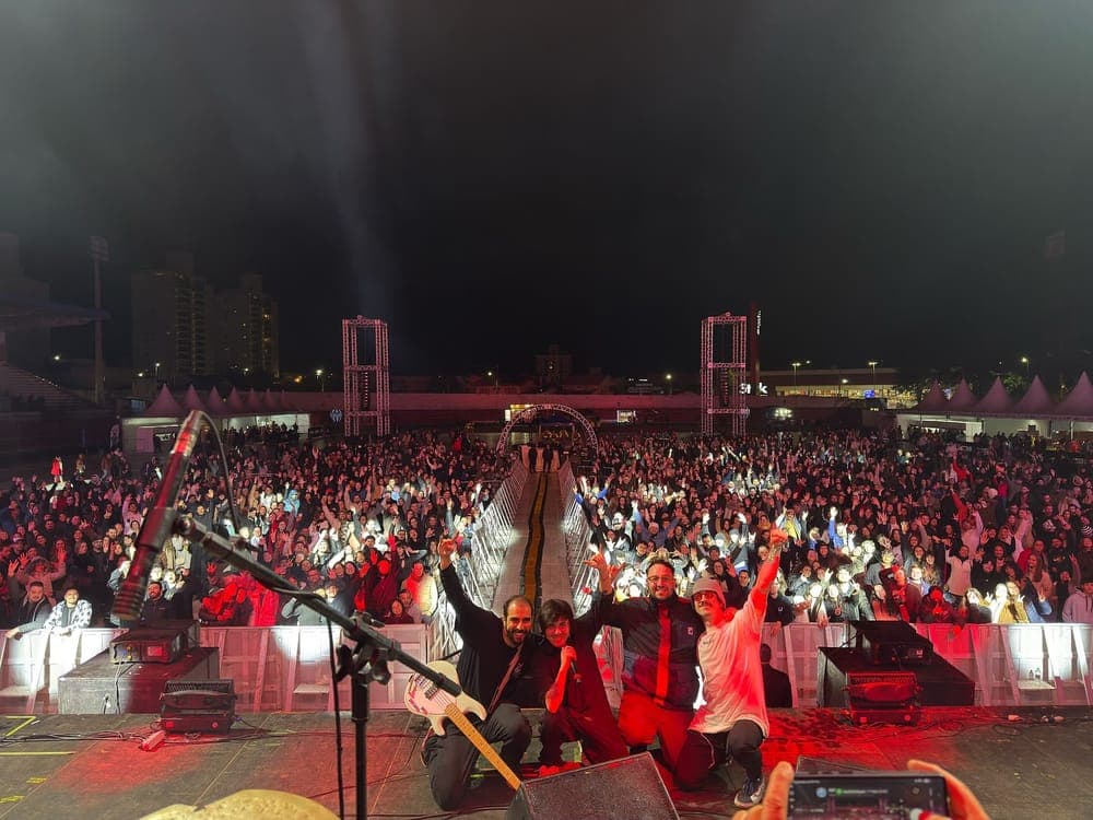 Banda no palco com o público lotando o espaço ao fundo